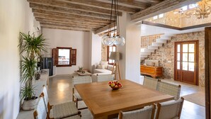 A spacious dining area with a wooden table and chairs, a potted plant, and a view of a staircase leading to a balcony.