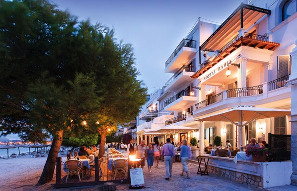 A beachfront hotel with outdoor seating and a sign reading "HOSTAL BAHIA".