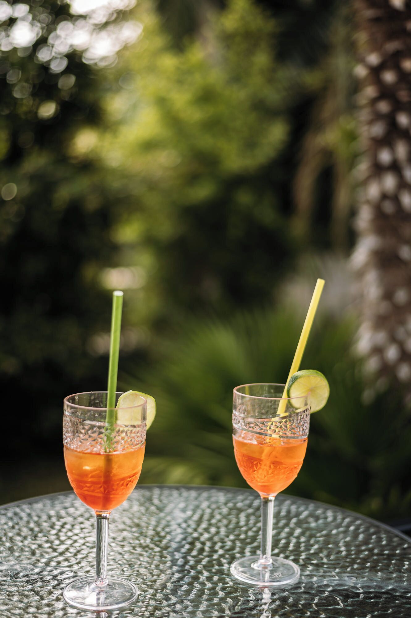 Two cocktails on a textured table with a blurred green background.