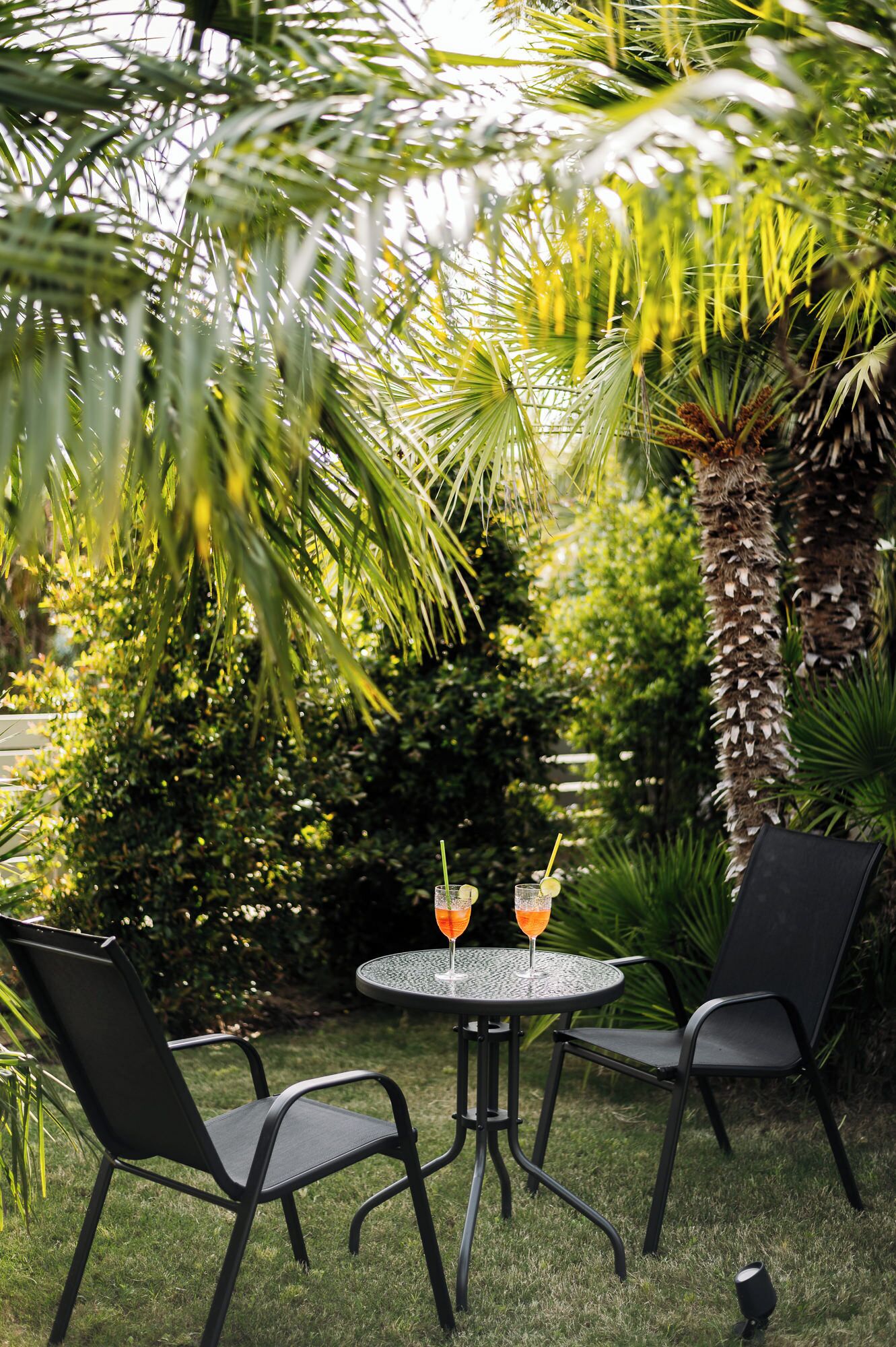 A round table with two chairs, two glasses with drinks, and a small speaker on the grass.