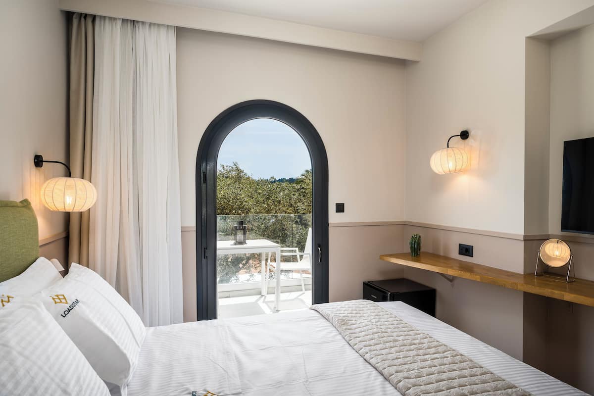 Ein Hotelzimmer mit Bett, Schreibtisch, einem Balkon mit Tisch und Stühlen sowie zwei Wandlampen.