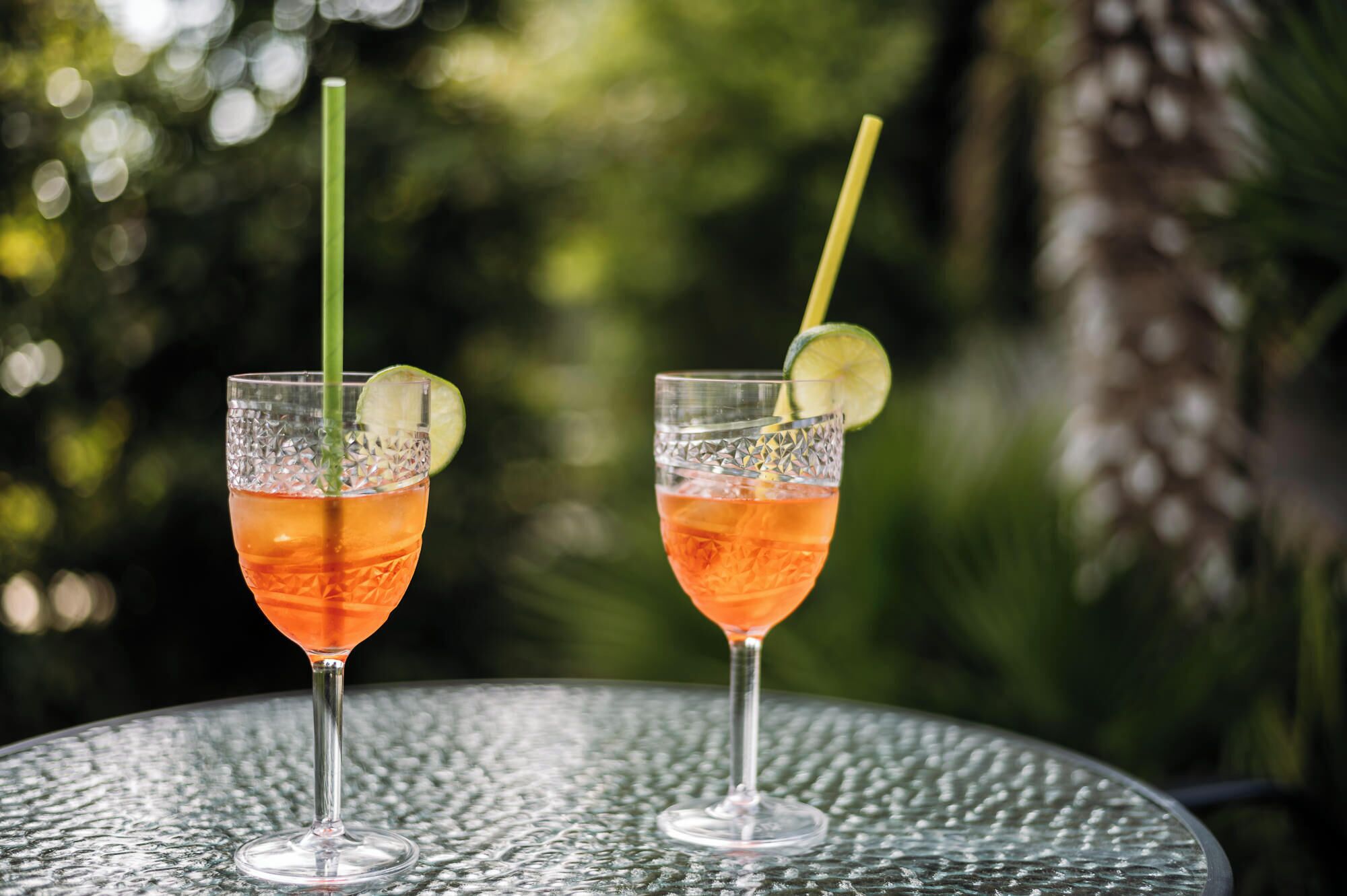 Two glasses of a red beverage with lime slices and straws on a textured outdoor table.