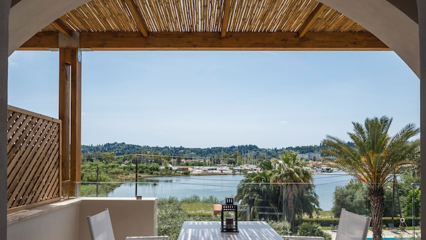 A balcony with a view of a lake and cityscape, furnished with a table and chairs. - Loadstar Rooms & Suites  (Corfu)