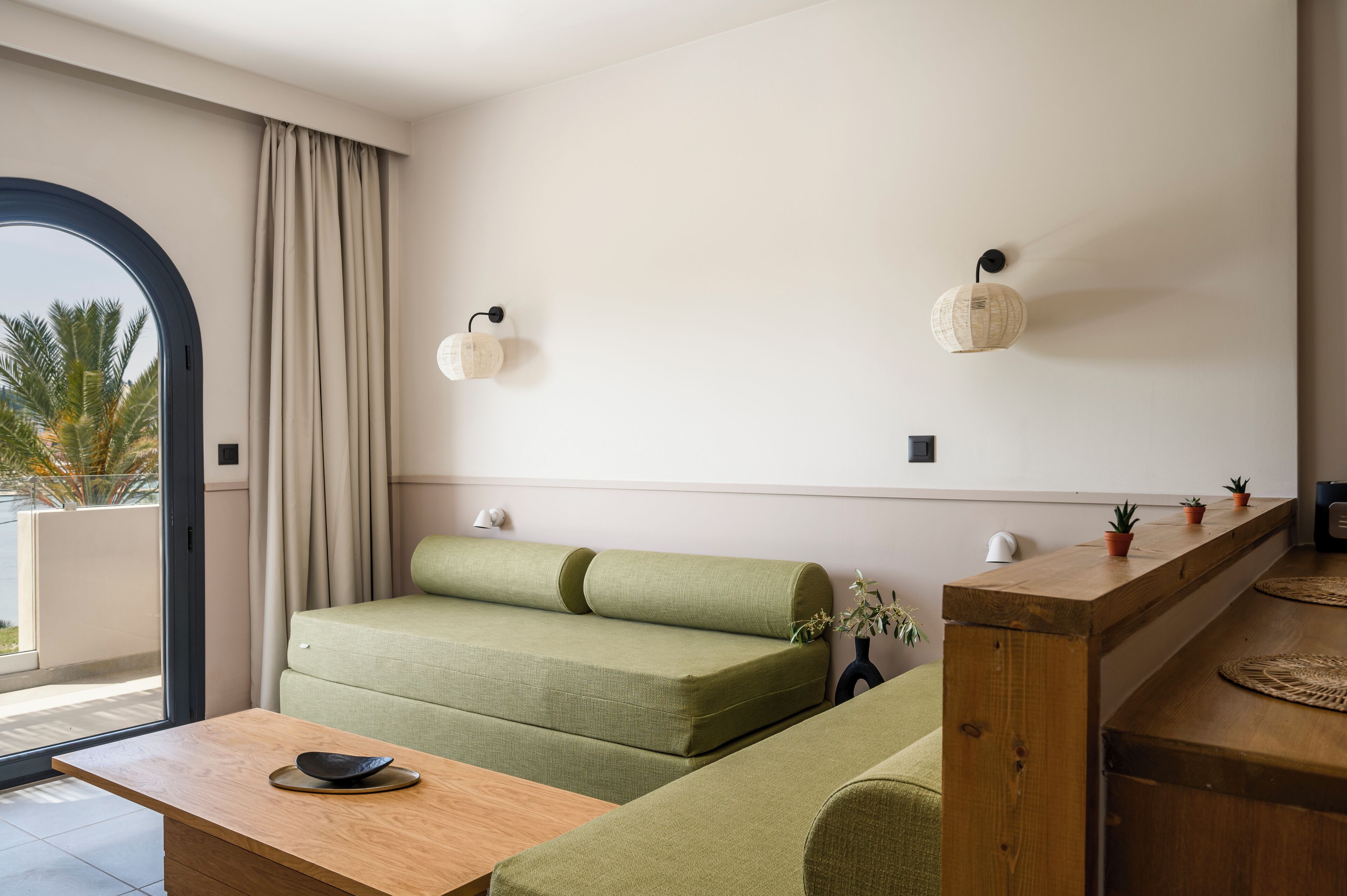 Una sala moderna con un sofá verde, una mesa de centro de madera y una pequeña cocina con mostrador de madera.