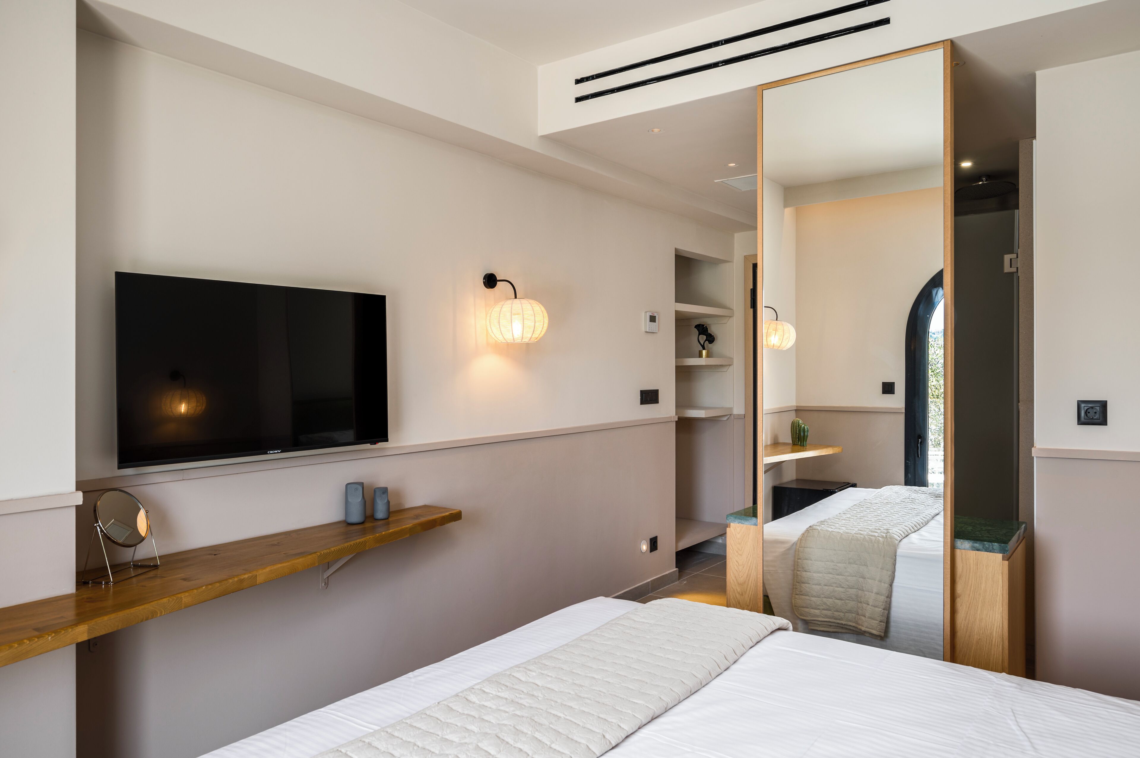 Una camera da letto moderna con un letto grande, una TV a parete, uno scaffale in legno e uno specchio.