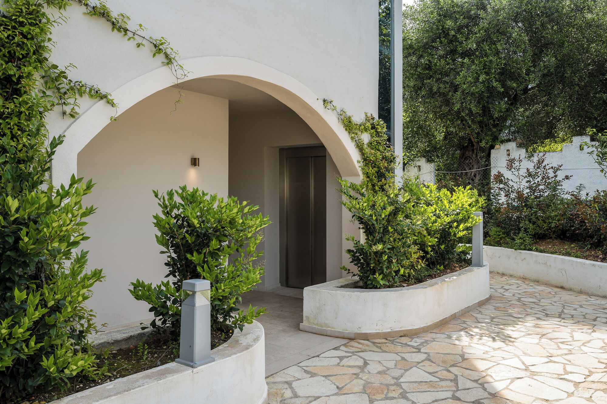 Une cour avec un mur blanc, une porte en arc de cercle et des plantes en pot.