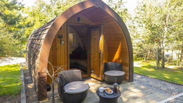 A cozy wooden cabin with a curved roof, two wicker chairs, a small table with a cup and a plate, and a coffee pot. - Wee Oak Tree Luxury Lodge with private hot tub (Drymen)