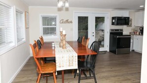 Un comedor con una mesa y sillas de madera, una araña y una cocina al fondo.