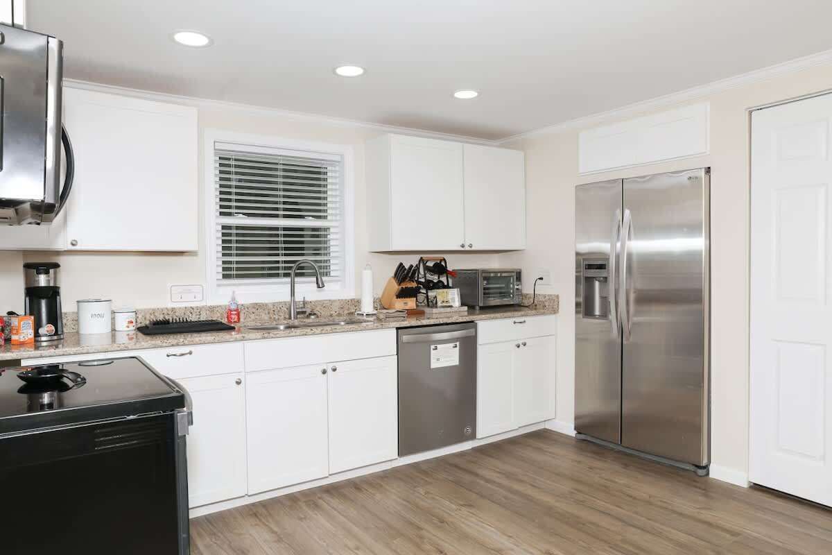 A modern kitchen with white cabinets, stainless steel appliances, and a window with blinds.