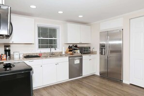 A modern kitchen with white cabinets, stainless steel appliances, and a window with blinds.