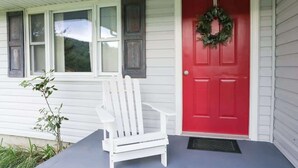 Una casa de madera blanca con una puerta roja y una silla blanca afuera.
