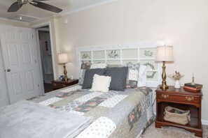 Une chambre à coucher comprenant un lit, deux tables de chevet, une commode, un ventilateur de plafond et une porte.