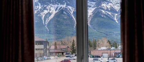 A view through a window of a parking lot with cars, buildings, and snow-capped mountains in the background.