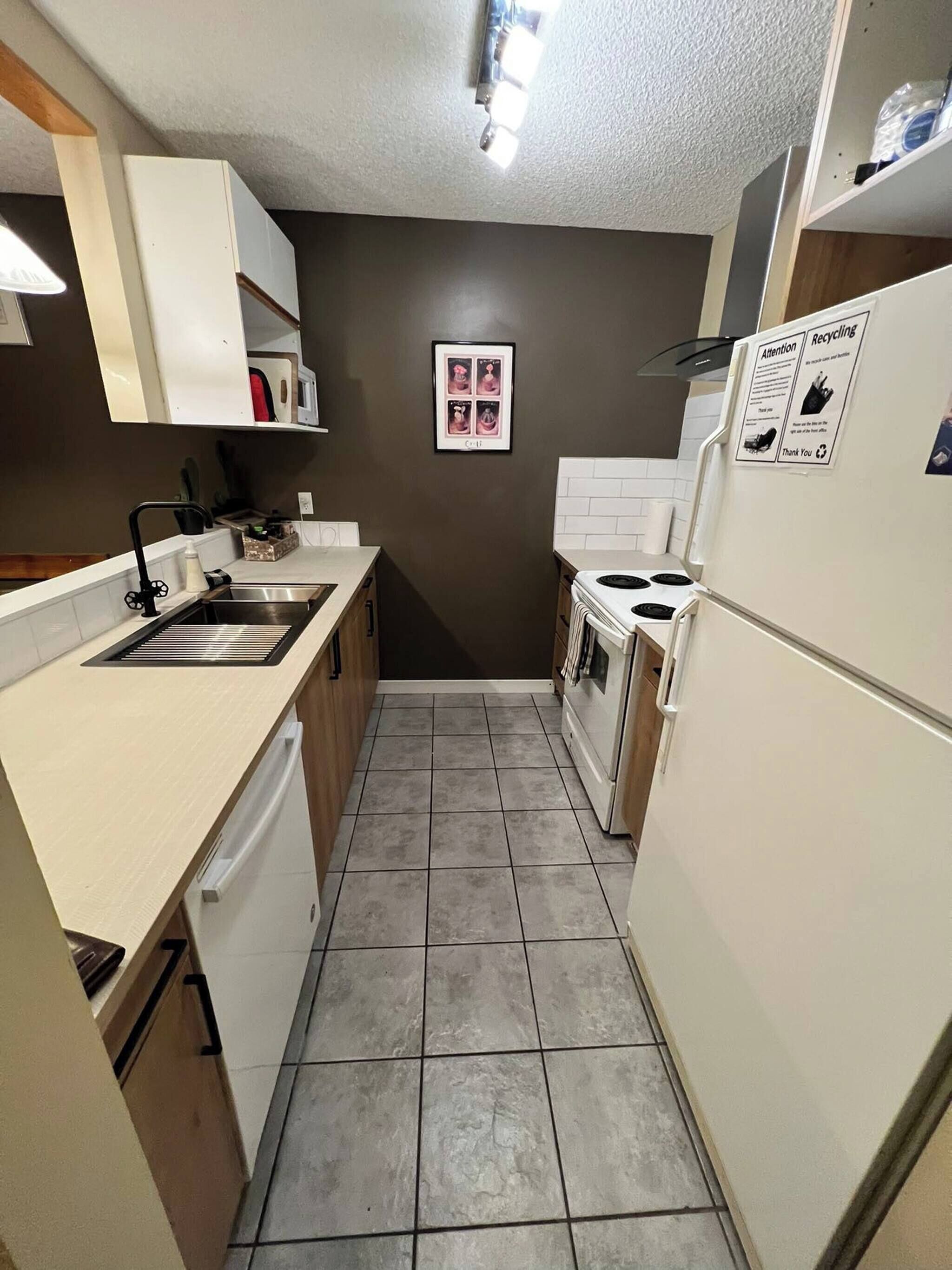 A compact kitchen with a sink, stove, and refrigerator, featuring a tiled floor and a framed picture on the wall.
