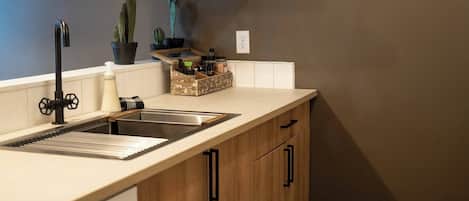 Una cocina con un lavamanos, armarios de madera, una encimera, una planta en maceta y un cuadro en la pared.