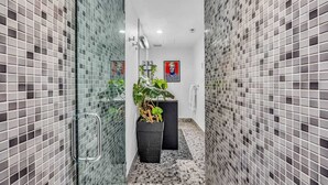 Um banheiro estreito com paredes revestidas de azulejos, box de vidro e uma planta em vaso.
