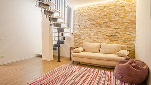 Un salon moderne avec un canapé beige, un tapis à motifs, un mur en pierre et un escalier au design minimaliste.