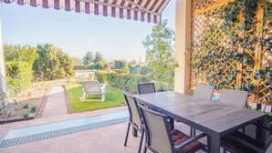 Une terrasse extérieure avec une table et des chaises, un petit jardin et une structure en treillis de bois.