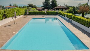 Une piscine rectangulaire bordée d’une terrasse carrelée, entourée de haies soigneusement taillées et agrémentée de quelques parasols.