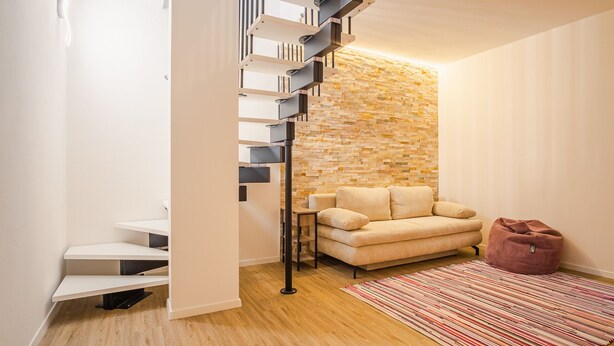 Un intérieur moderne avec un escalier, un canapé, un tapis et un mur en pierre.