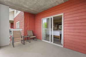 A room with a red exterior wall, a sliding glass door leading to a bedroom, and two chairs in the foreground. - Wake Up to the River, Walk to the Fun - 3 BR Condo (Pigeon Forge)