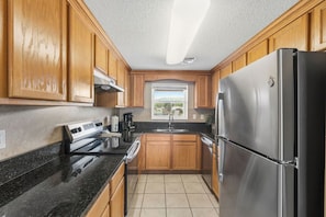 A kitchen with wooden cabinets, a stainless steel refrigerator, and a window with a view.