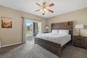 A bedroom with a bed, a ceiling fan, a nightstand, a lamp, and a painting on the wall.