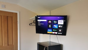 A flat-screen TV mounted on a wall above a white cabinet, displaying a Roku interface with various streaming channels. - Impeccable 1-bed Lodge in Eastleigh (Eastleigh)