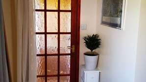 A room with a wooden door with frosted glass panels, a white wall with a framed picture, and a small white nightstand with a potted plant. - Impeccable 1-bed Lodge in Eastleigh (Eastleigh)