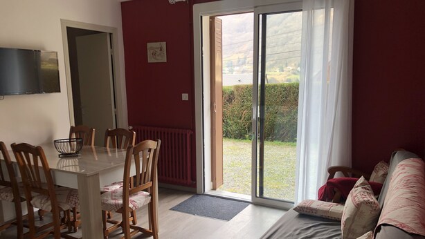 Ein Essbereich mit Tisch und Stühlen, einer Couch mit Kissen und einer Glastür zum Garten.