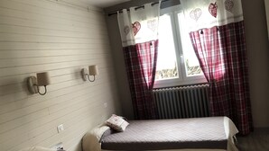 Ein Zimmer mit zwei Einzelbetten, einem Vorhangfenster und zwei Wandlampen.