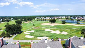 A golf course with sand bunkers, a pond, and residential buildings in the background. - RR7510 – Luxury 6BR Villa w/ Pool, Hot Tub & Game Room on Reunion Golf Course (Kissimmee)