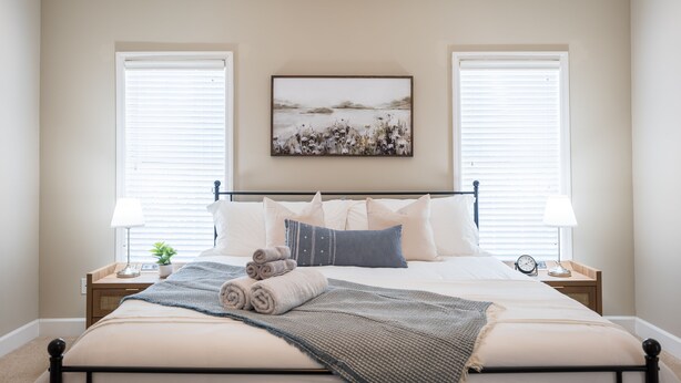 A bedroom with a bed, two bedside tables, a wall-mounted painting, and a window with blinds.