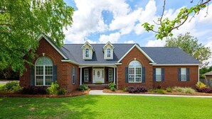 A two-story brick house with a front porch, a garage, and a well-maintained lawn.