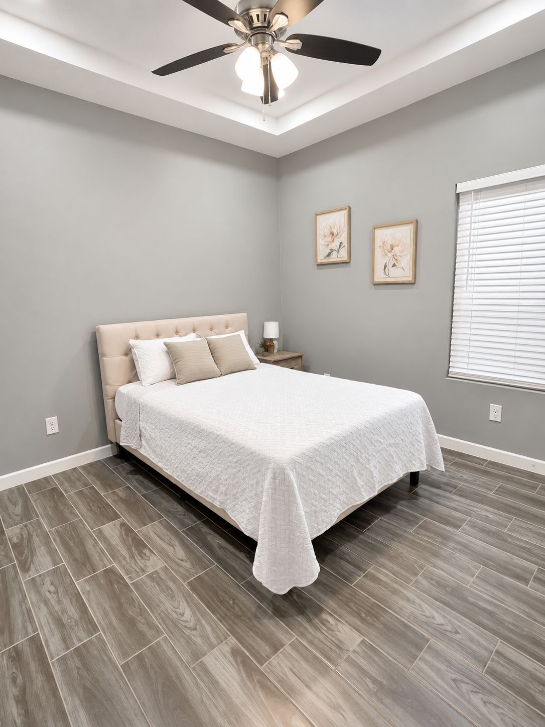 A bedroom with a bed, a ceiling fan, a nightstand, and a window with blinds.