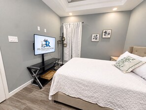 Ein modernes Schlafzimmer mit Bett, Fernseher, Nachttisch und Wandregal.