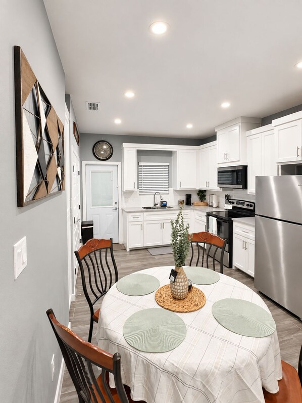 A modern kitchen with white cabinets, stainless steel appliances, and a dining area with a round table and chairs.