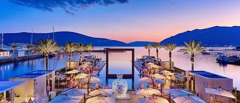 A waterfront resort with outdoor seating, palm trees, and boats.