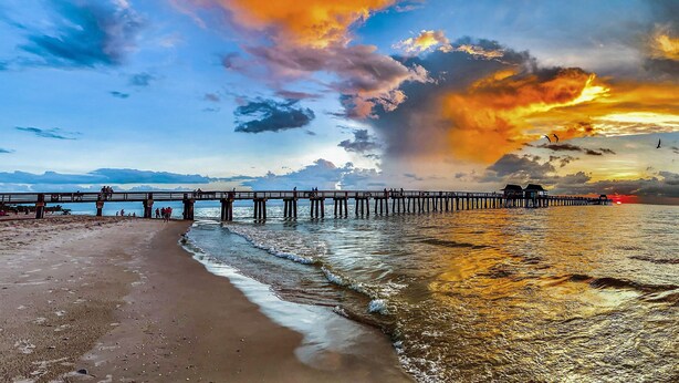 Eine Pier, die sich in ruhiges Wasser erstreckt, mit einem Sonnenuntergang im Hintergrund.