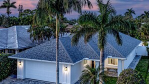 A modern house with a grey tiled roof, surrounded by well-maintained gardens and palm trees. - Tee, Splash & Relax | Putting Green, Pool, Spa (Naples)