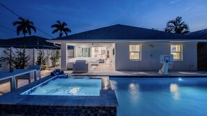 A modern house with a swimming pool, outdoor furniture, and a well-lit interior. - Tee, Splash & Relax | Putting Green, Pool, Spa (Naples)