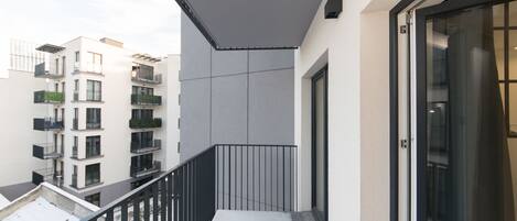 Ein Balkon mit Metallgeländer, einer Tür und Blick auf angrenzende Gebäude.