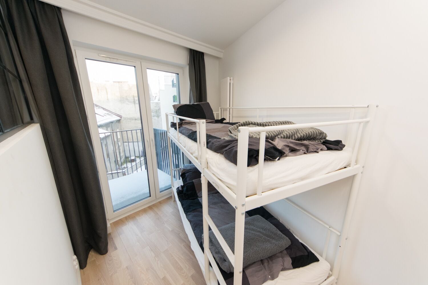 Quarto estilo dormitório com beliche, porta de correr para varanda e radiador na parede.