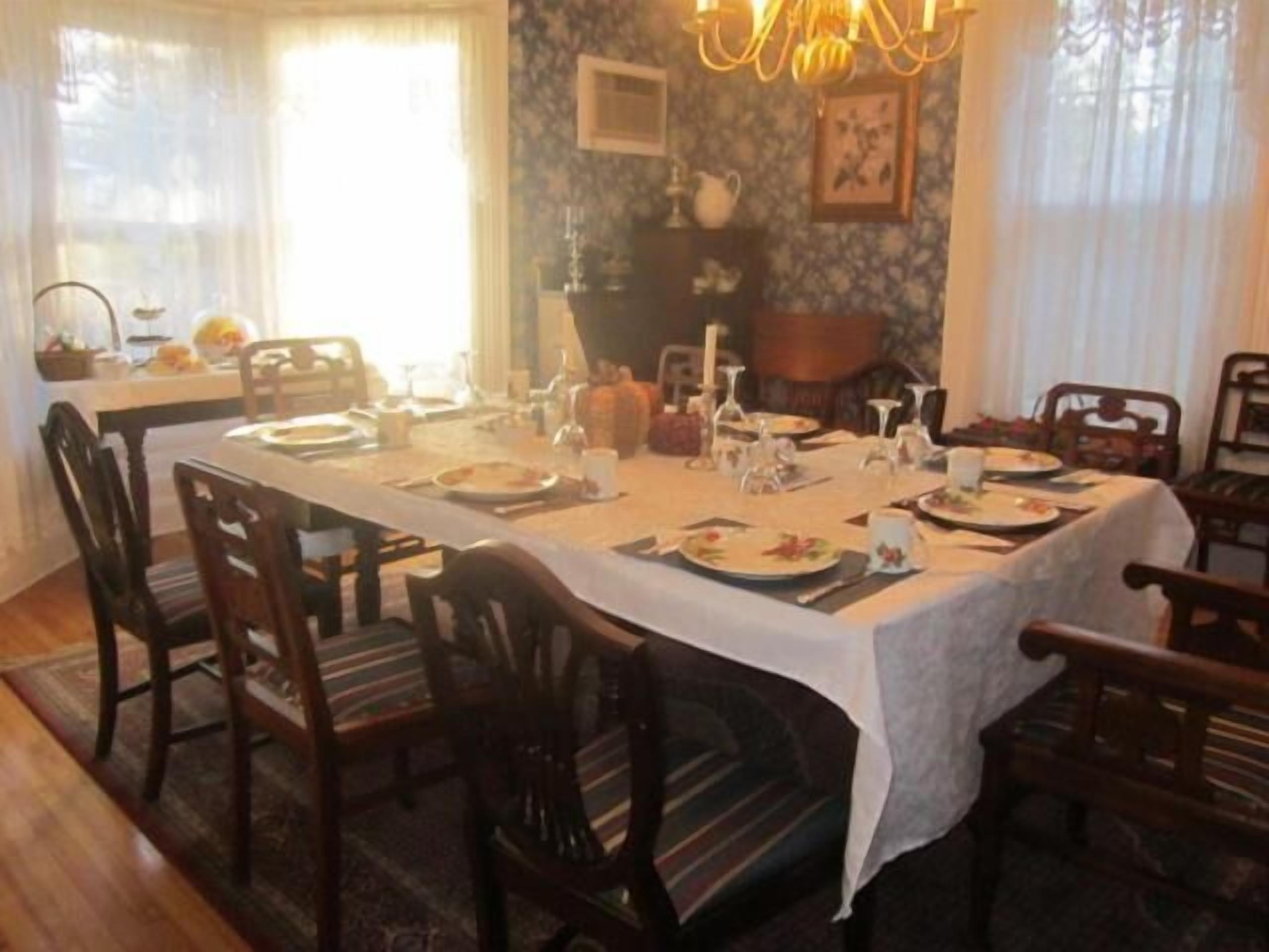 A dining room with a long table set for a meal, surrounded by wooden chairs.