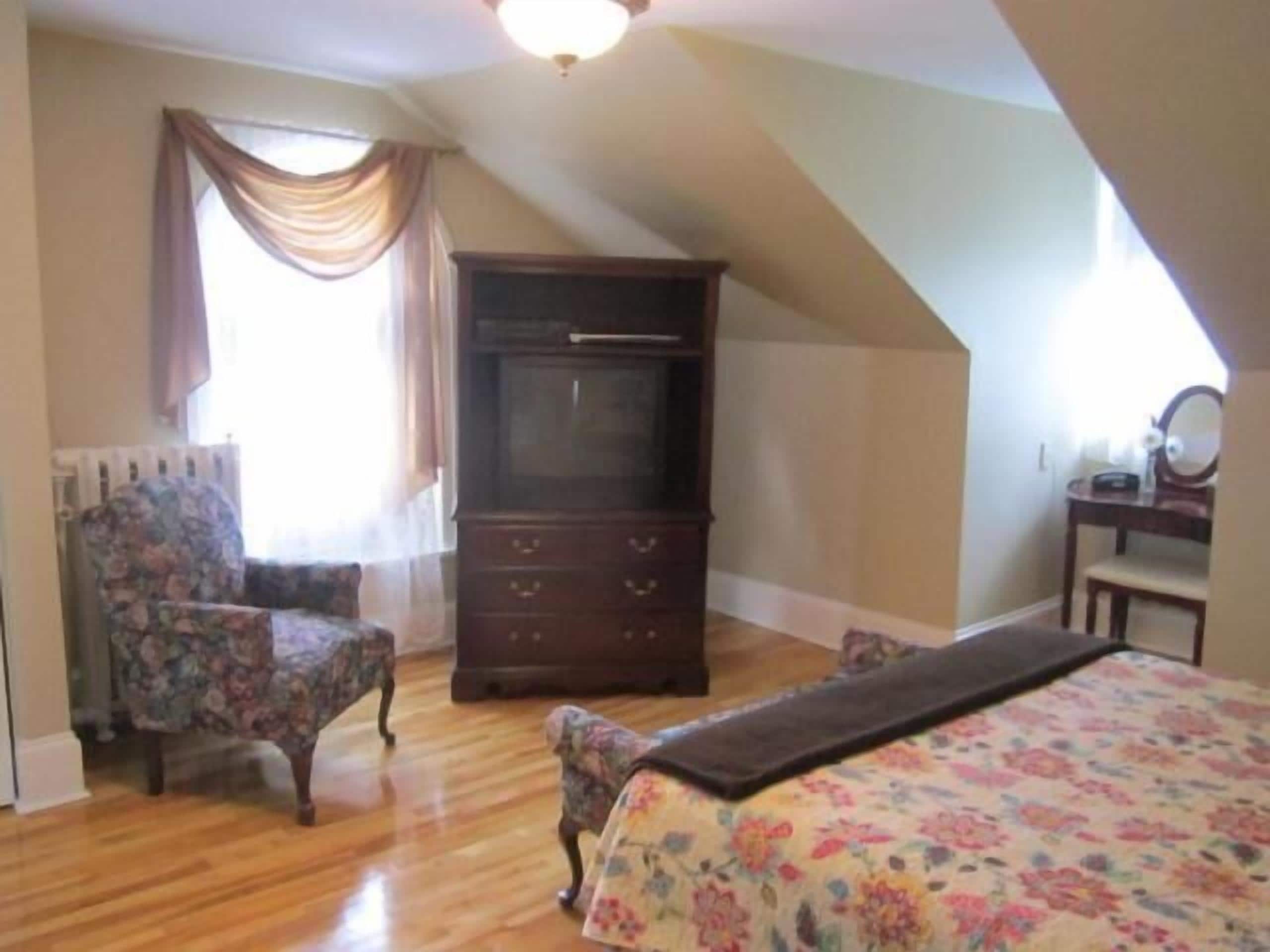 Une chambre à coucher avec une commode en bois, une couvre-lit à motifs floraux et une chaise.