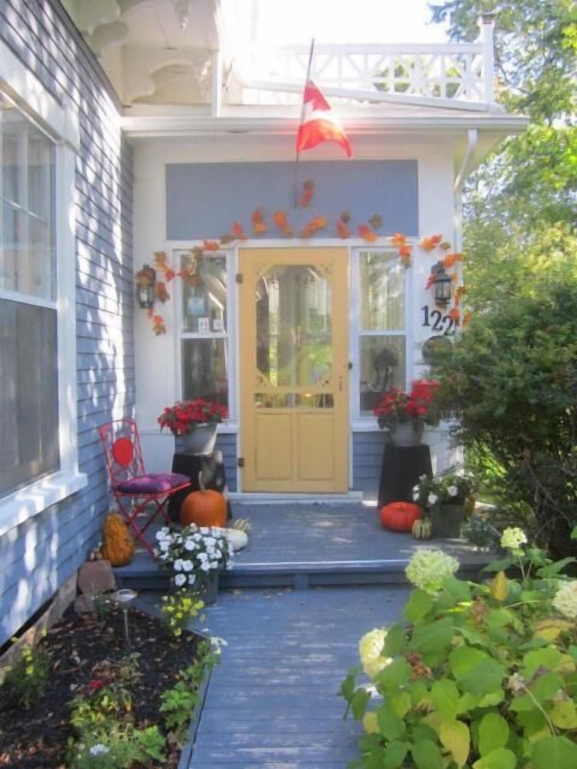 Uma casa com fachada azul, porta amarela e varanda decorada com folhas de outono e abóboras.