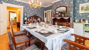 Comedor con una mesa grande dispuesta para seis personas, rodeada de sillas de madera con cojines a rayas. Un candelabro cuelga del techo, y un espejo está montado en la pared sobre la mesa.