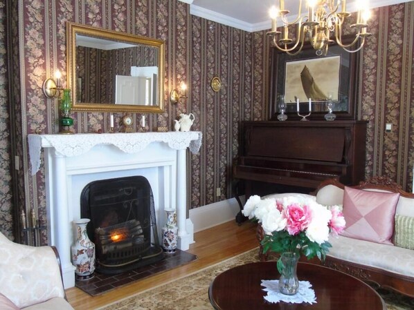 A living room with a fireplace, a piano, and a sofa. - The Dawson House Bed & Breakfast (Charlottetown)