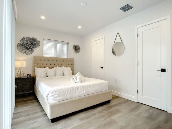 Un dormitorio con una cama grande, una mesita de noche, un reloj de pared y una puerta.