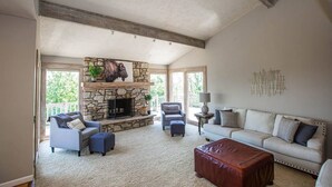 A spacious living room with a stone fireplace, a white sofa, and a leather ottoman. - Lakeview Luxury - Deck With View, 3 Family Rooms (Manhattan)